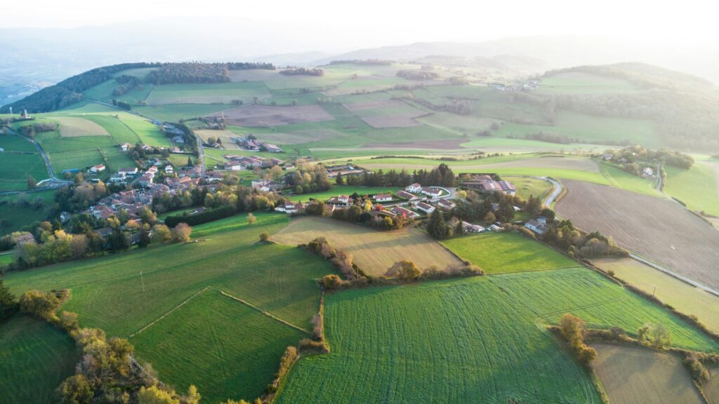 Luftbild einer Hügellandschaft mit Dorf, Wiesen, Äckern und Hecken